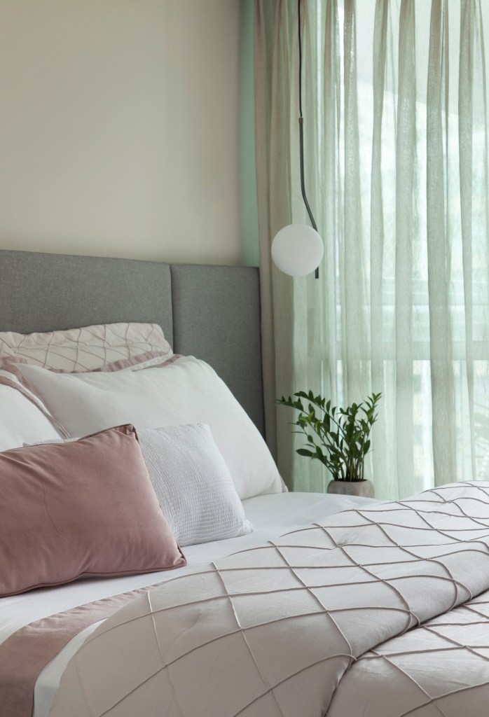Quarto com cama de casal, cabeceira acolchoada, luminária lateral esférica e cortina clara.