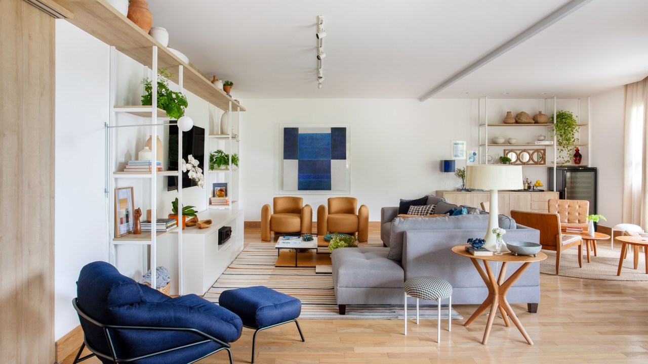 Sala de estar clara com piso em madeira, estante branca, poltrona azul, sofá cinza.