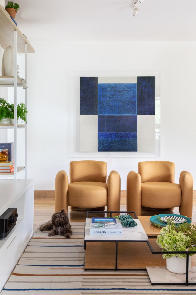 Sala de estar com duas poltronas em tom bege; quadro azul na parede.