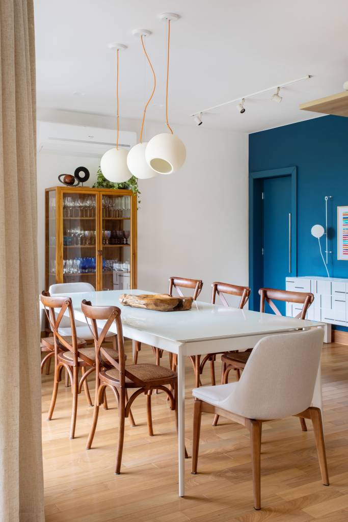 Sala de jantar integrada com cozinha; mesa branca e cadeiras de madeira; parede azul