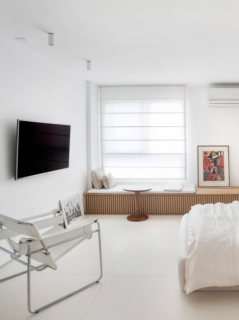 Loft branco com cama branca baixa e banco de madeira ripada
