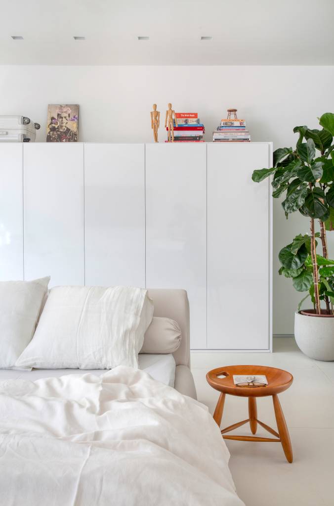Quarto branco com cama baixa; ficus; armário branco.