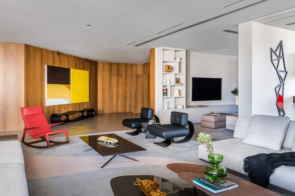 Sala de estar com poltronas de design, tapete claro, mesas de centro e parede revestida de madeira.