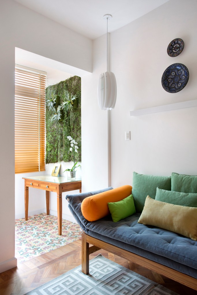 Sala com varanda e sofá pequeno com almofadas coloridas.