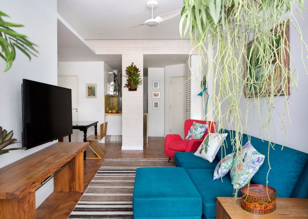 Sala de estar pequena com tapete listrado e sofá azul turquesa; poltrona vermelha.