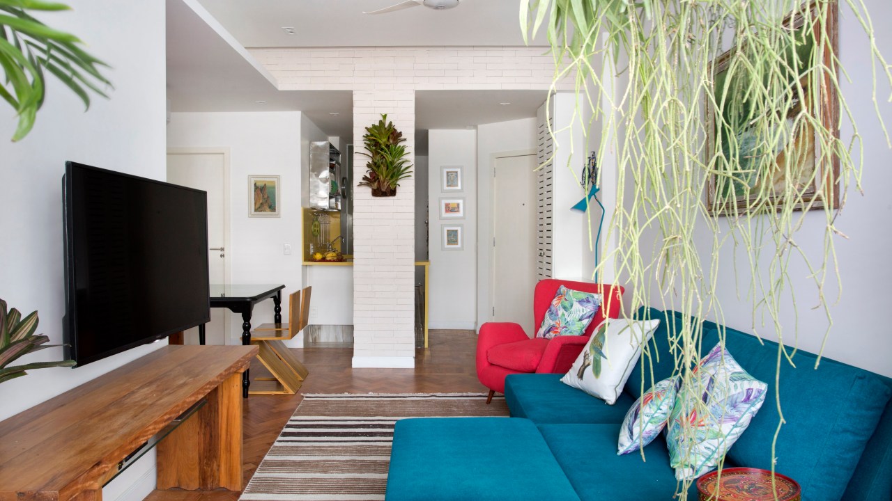 Sala de estar pequena com tapete listrado e sofá azul turquesa; poltrona vermelha.