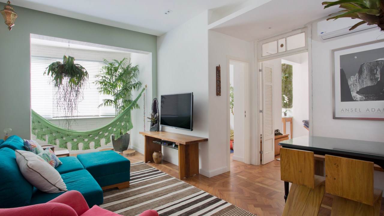 Sala de estar pequena com sofá azul turquesa, tapete listrado e rede.