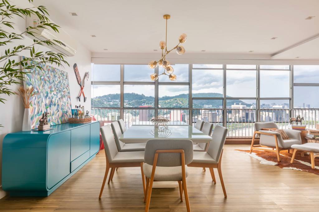 Sala de jantar com piso vinilíco, buffet azul, mesa com tampo branco e lustre.