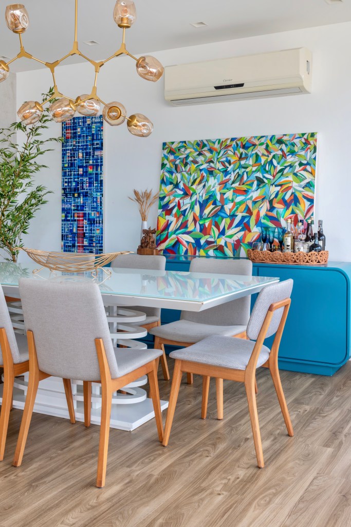 Sala de jantar com piso vinilíco, buffet azul, mesa com tampo branco e lustre.