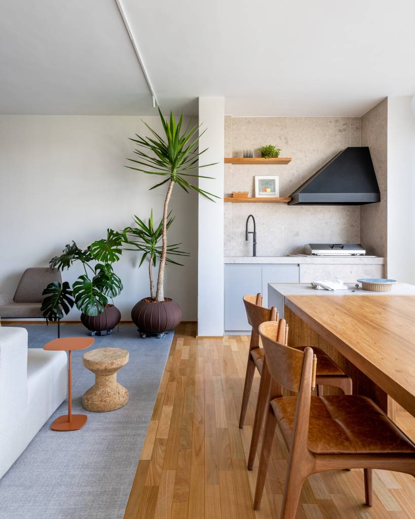 Sala de estar integrada com varanda e churrasqueira; piso de madeira e mesa de madeira.