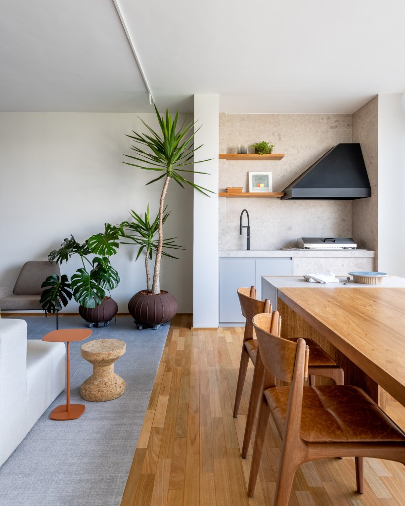Sala de estar integrada com varanda e churrasqueira; piso de madeira e mesa de madeira.