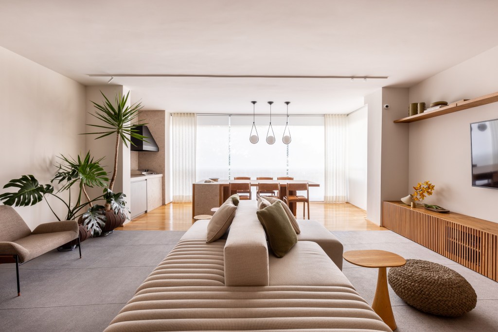 Sala integrada com varanda em tons neutros; sofá ilha claro e plantas.