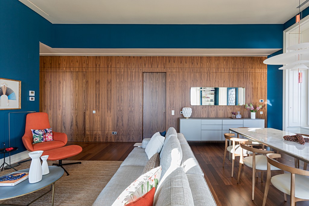 Sala de estar integrada com sofá cinza e paredes azuis.