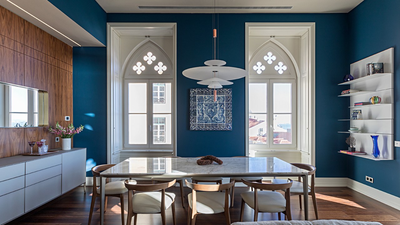 Sala de jantar com paredes azuis, mesa com tampo de mármore e luminária branca.