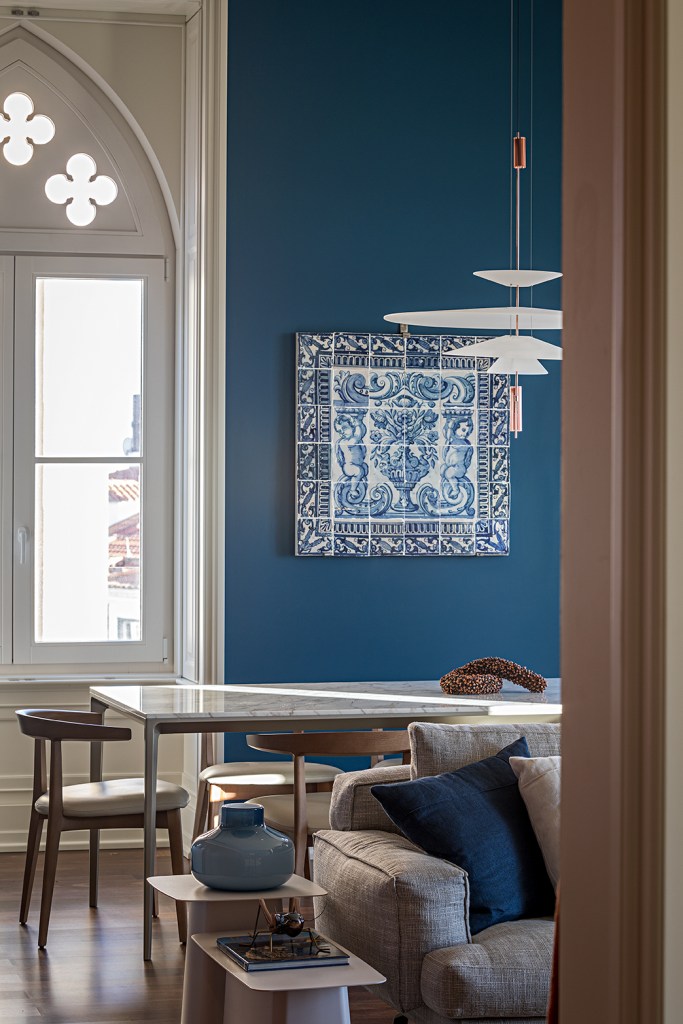 Sala de jantar com paredes azuis, mesa com tampo de mármore e luminária branca.