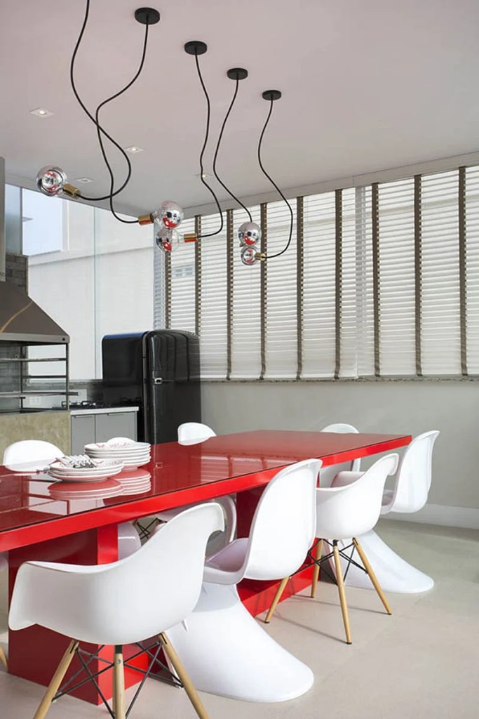 Área gourmet com mesa vermelha e composição de cadeiras brancas.