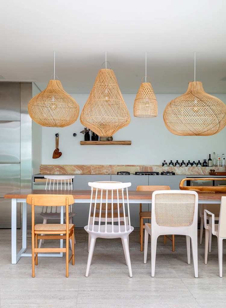 Sala de jantar com mesa de madeira e composição de cadeiras de materiais diferentes; luminárias de palhinha.