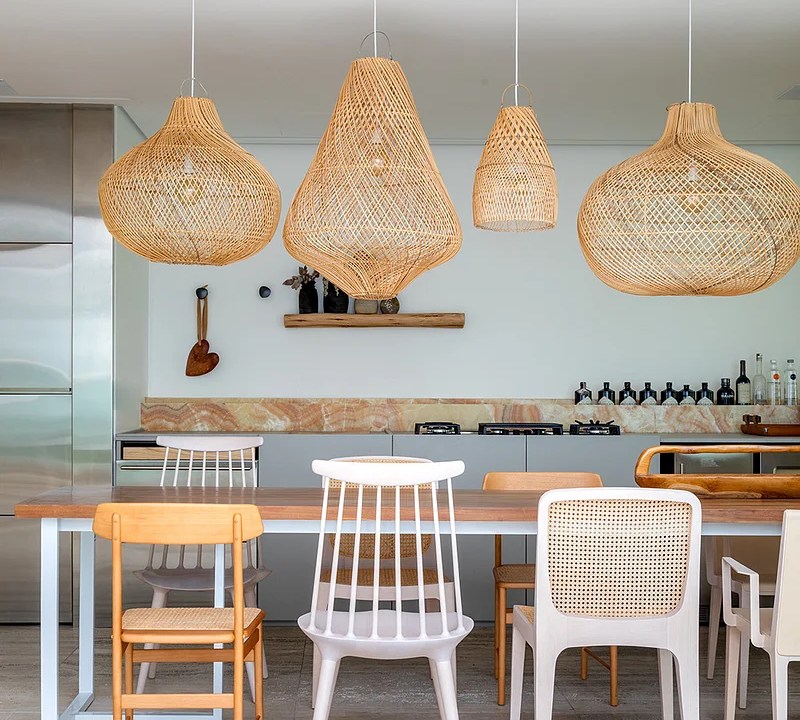 Sala de jantar com mesa de madeira e composição de cadeiras de materiais diferentes; luminárias de palhinha.