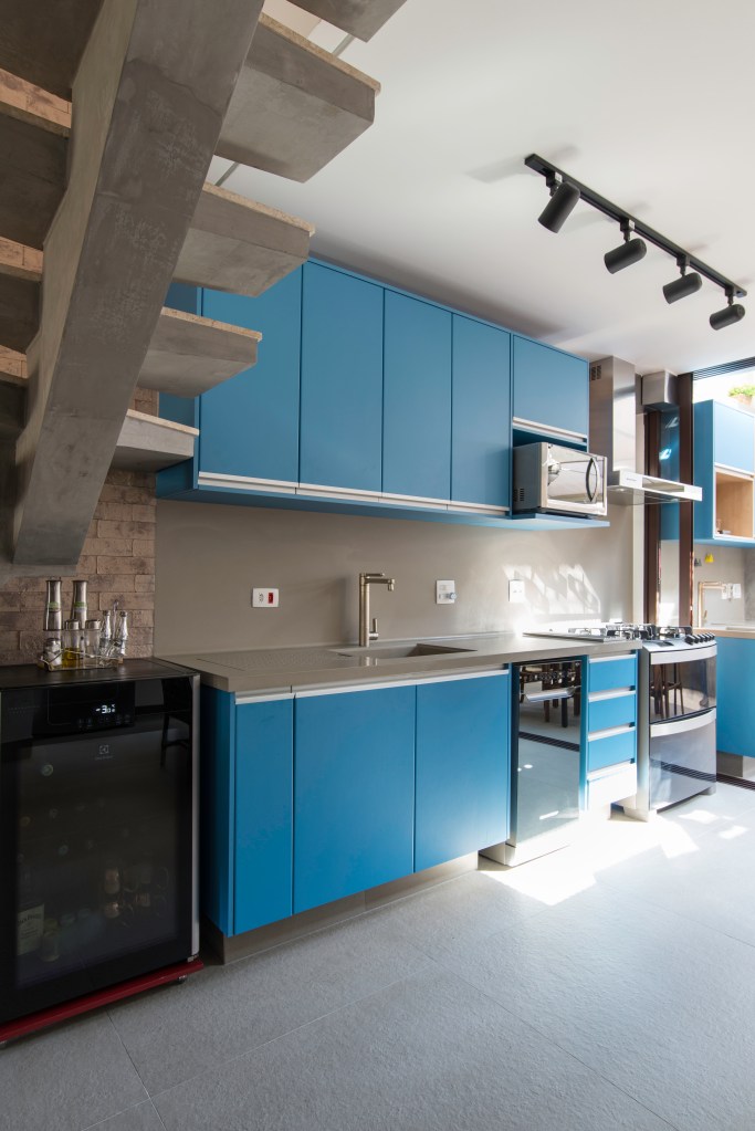 Cozinha com marcenaria azul com mesa de madeira voltada para quintal