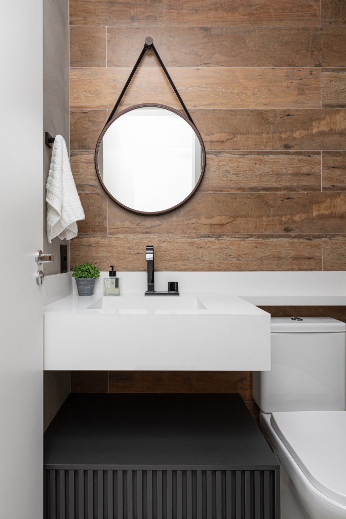 Banheiro com revestimento de madeira e espelho redondo.