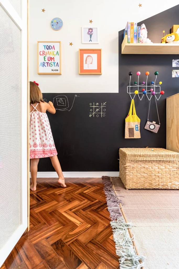 Quarto infantil com parede de quadro negro e cabideiro com ganchos coloridos.