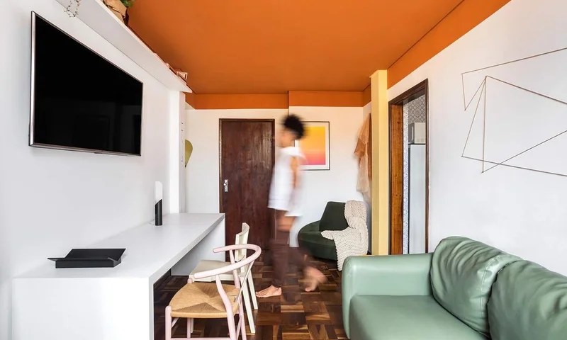 Sala de estar com teto colorido laranja; sofá verde e aparador branco.