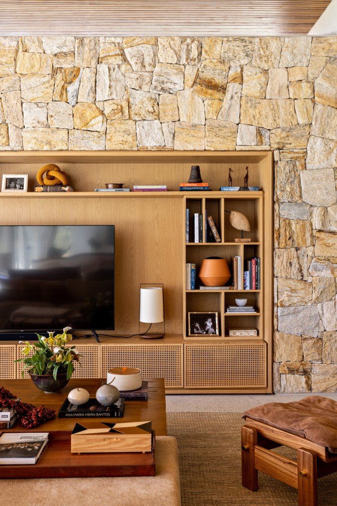 Sala de tv com parede de pedra e estante de madeira com nichos.