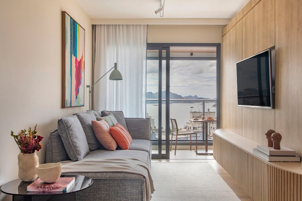 Sala de estar; sala de tv com sofá cinza, almofadas coloridas, luminária de piso e paredes revestidas de madeira.