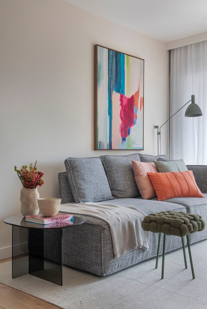 Sala de estar com sofá cinza e almofadas coloridas; quadro na parede em cima do sofá.