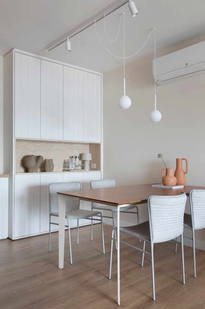 Sala de jantar branca com mesa retangular de madeira e cadeiras brancas.