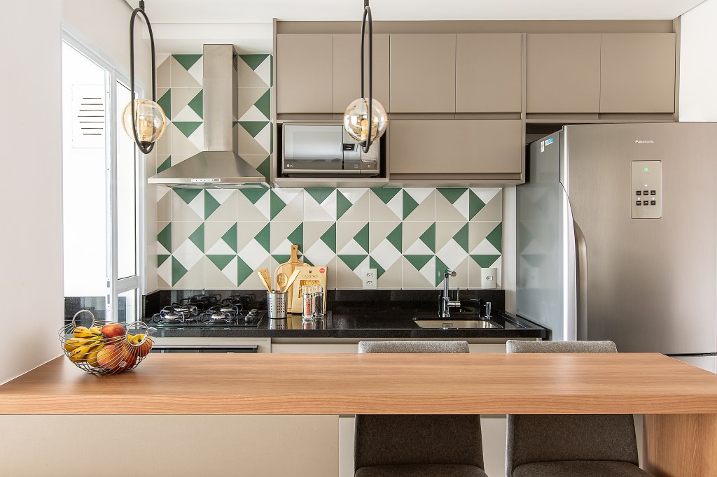 Cozinha americana; cozinha integrada com backsplash de azulejos verdes, brancos e cinzas. Bancada de mardeira.