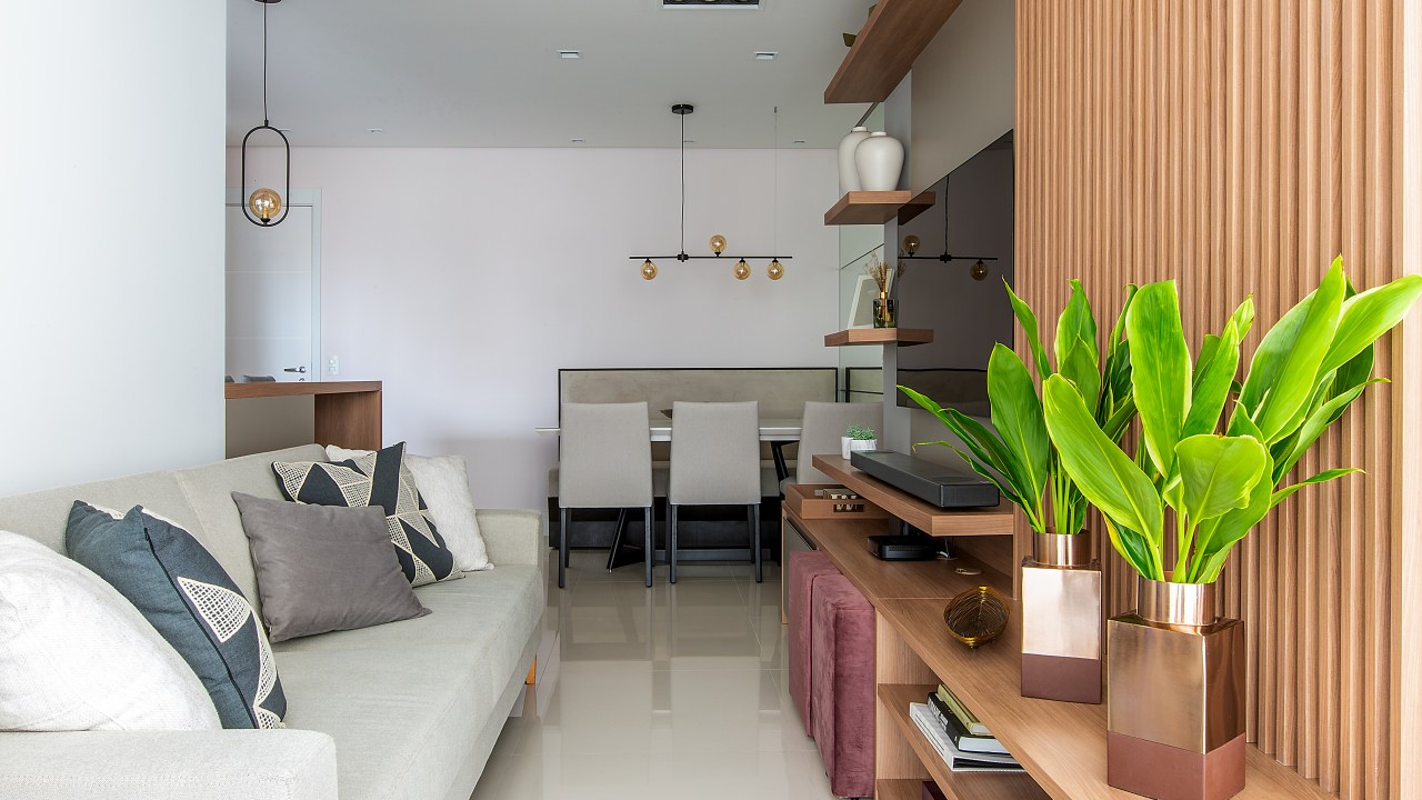 Sala de estar e jantar integradas com sofá cinza, rack de madeira e mesa de jantar branca.