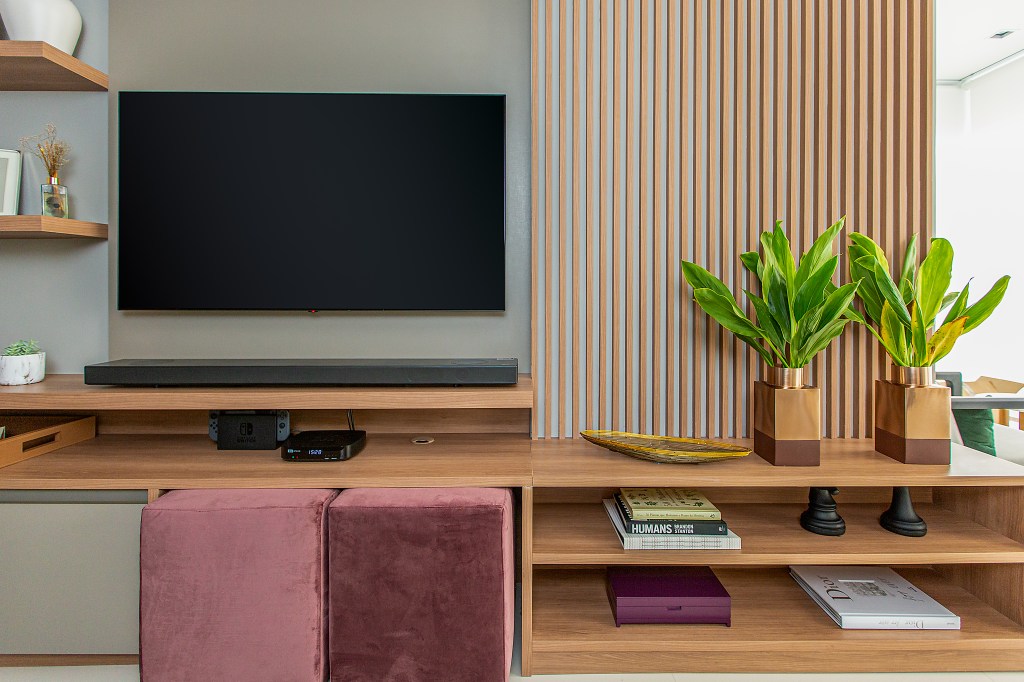Sala de tv com painel de madeira ripada, rack de madeira e pufe na cor berinjela.
