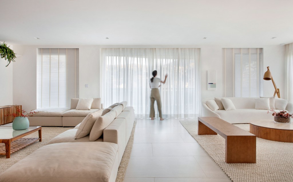 Sala minimalista em tons claros com cortinas brancas e sofás brancos.