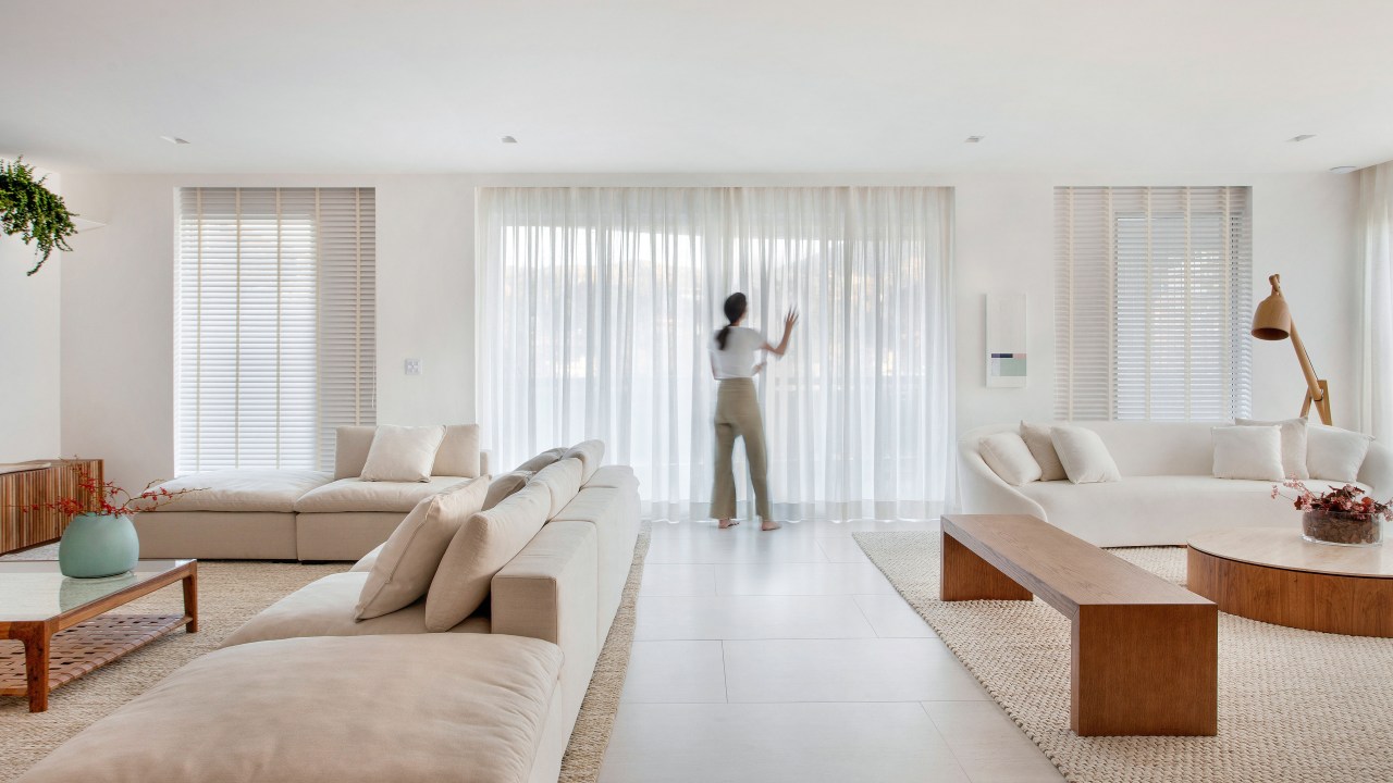 Sala minimalista em tons claros com cortinas brancas e sofás brancos.