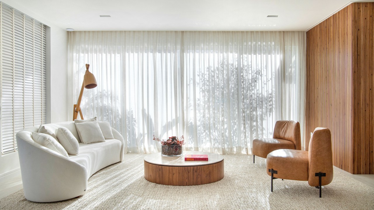 Sala minimalista em tons claros; sofá branco claro curvo, tapete claro, poltrona, mesa de centro.