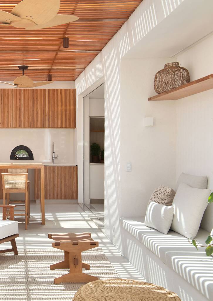 Área gourmet com cobertura de madeira ripada; banco branco esculpido na parede.