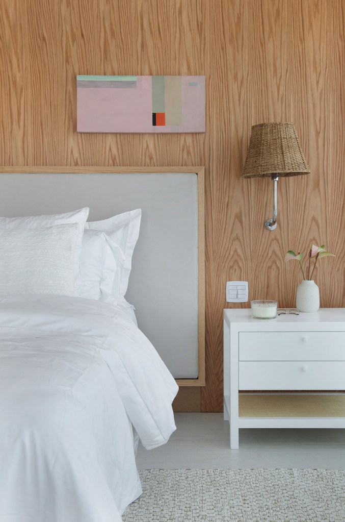 Quarto com parede revestida de madeira, cama de casal com roupa de cama branca.