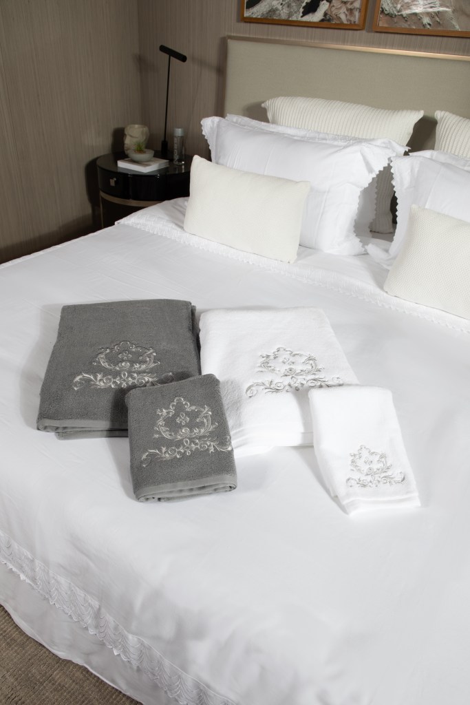 Cama com lençóis brancos; toalhas bordadas sobre cama.