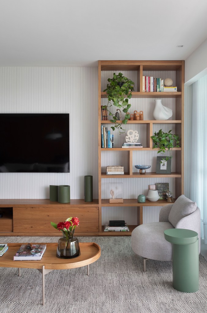 Sala de tv com sofá claro e estante vazada com plantas.