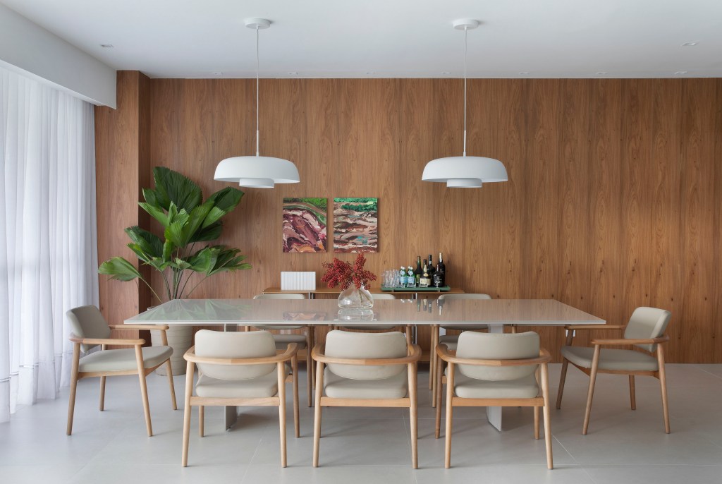 Sala de jantar com mesa de tampo em laca e luminárias brancas; parede revestida de madeira ao fundo.