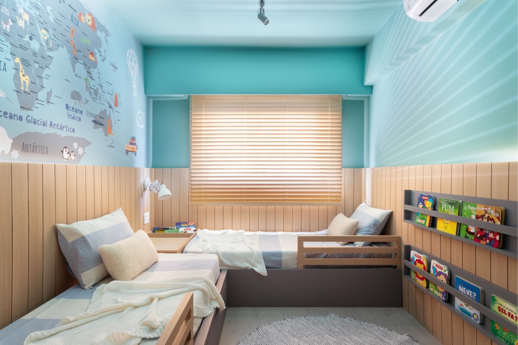 Quarto infantil com duas camas, parede azul e papel de parede com mapa múndi.