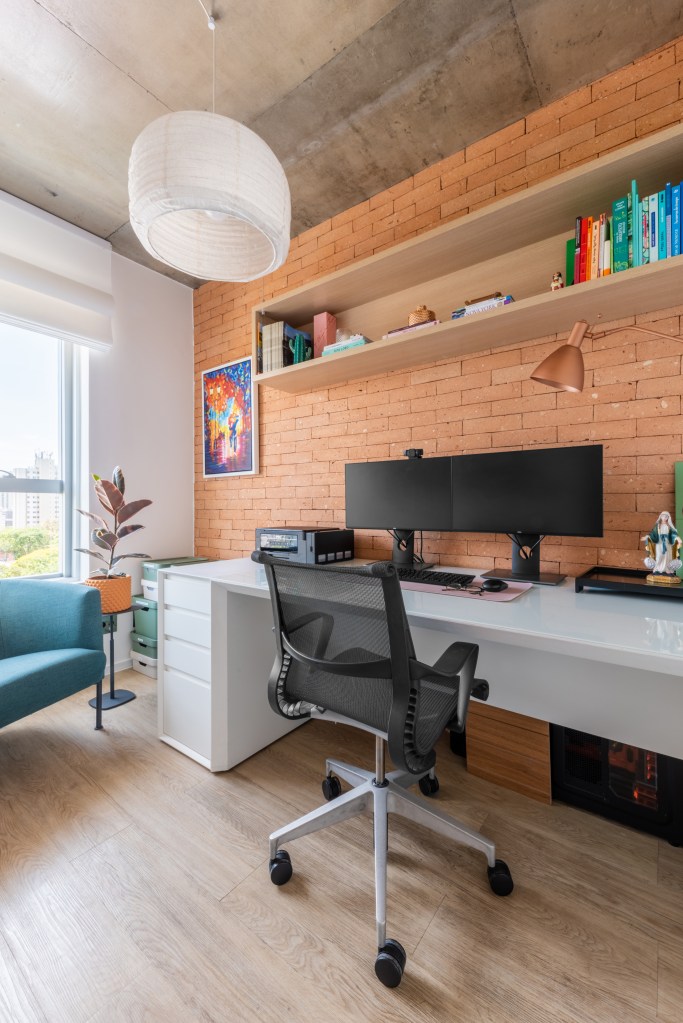 Home office em estilo industrial com mesa branca e parede de tijolinhos.