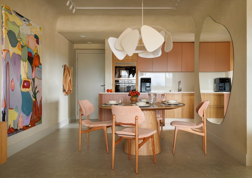 Sala de jantar integrada com cozinha; mesa redonda, cadeiras de madeira e luminária.