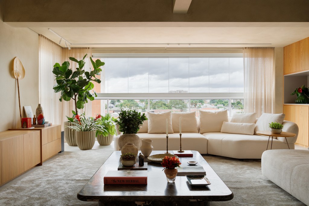 Sala de estar integrada com varanda; sofá branco, mesa de centro e plantas