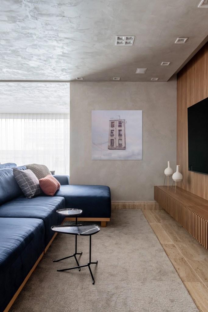 Sala de tv com parede revestida de cimento queimado e sofá azul