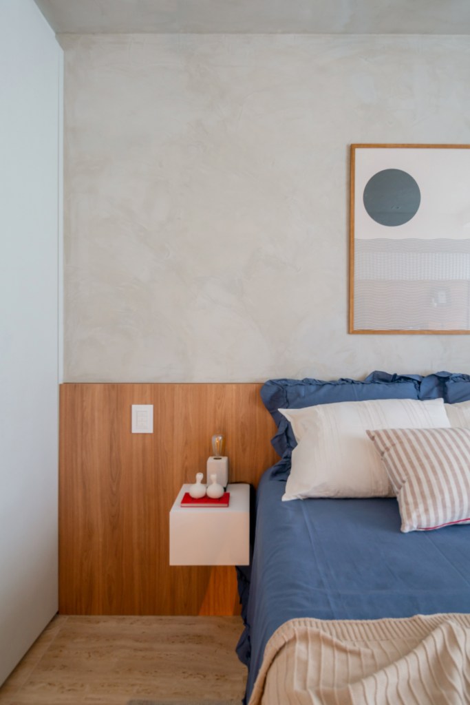 Quarto com cabeceira de madeira e cama de casal com roupa de cama azul; quadros em cima da cama
