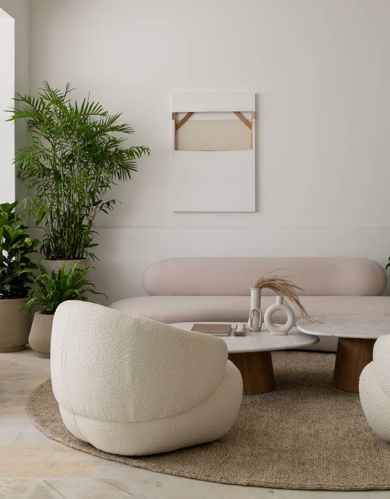 ape-100m-decor-natural-cantinho-de-leitura-isabella-lucena-07-sala-plantas Sala de estar com sofá branco curvo, duas poltronas brancas e mesa de centro em forma curva.