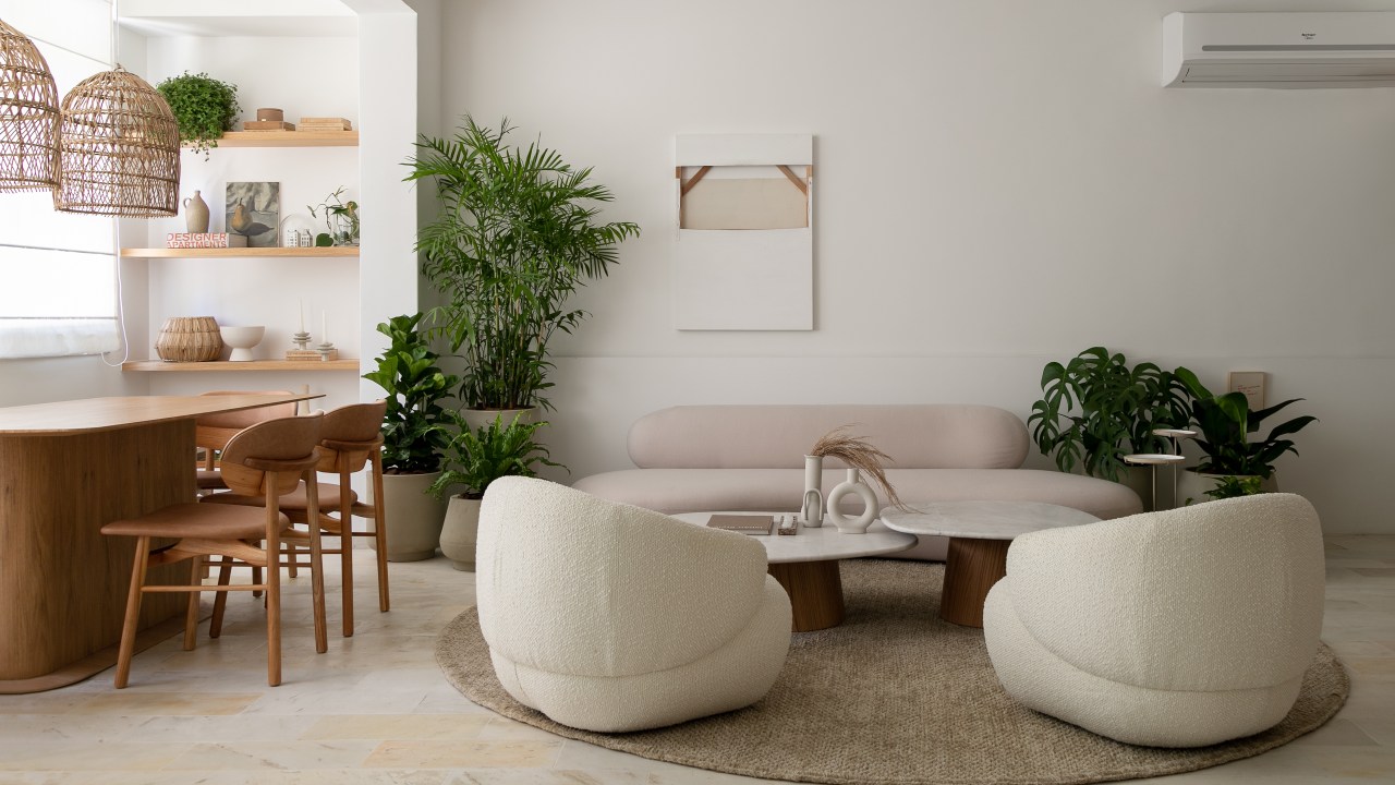 Sala de estar com sofá branco curvo, duas poltronas brancas e mesa de centro em forma curva.