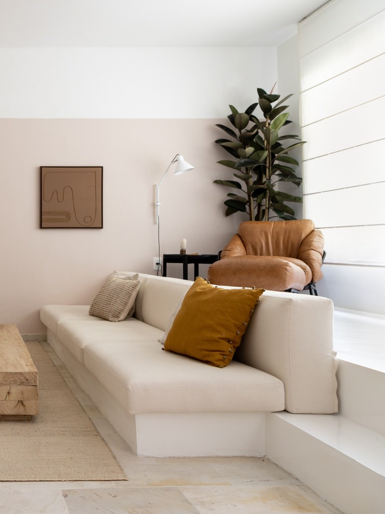 Sala de tv em tons claros com rack branco, sofá branco e mesa de centro de madeira rústica.